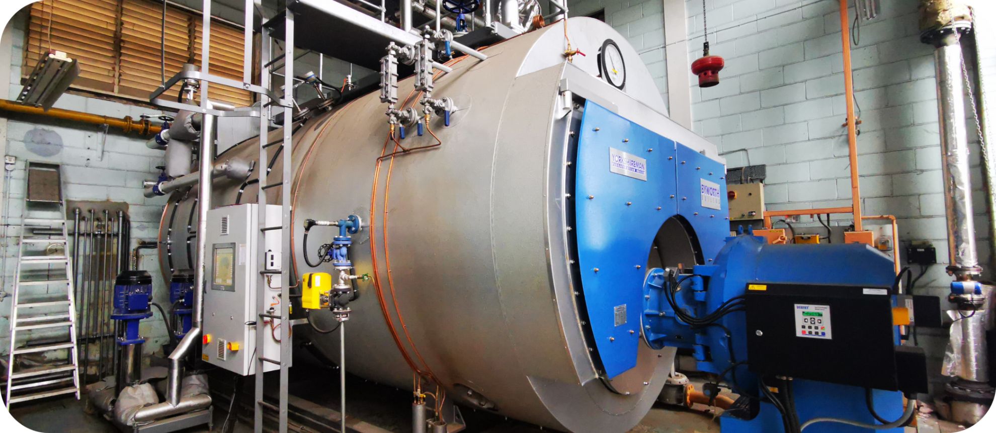 Industrial steam boiler with a Byworth logo in a factory. There is a blue burner mounted on the front